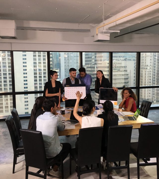 Professionals gathered around a table having na meeting. One person is holding a calendar to present information to the rest of the team.